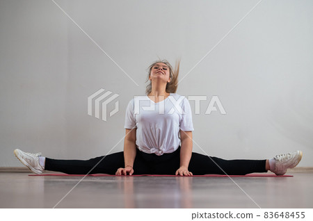 A young flexible fat woman sits in a transverse twine and waves her hair against a white background A young flexible fat woman sits in a transverse twine and waves her hair against a white background 83648455
