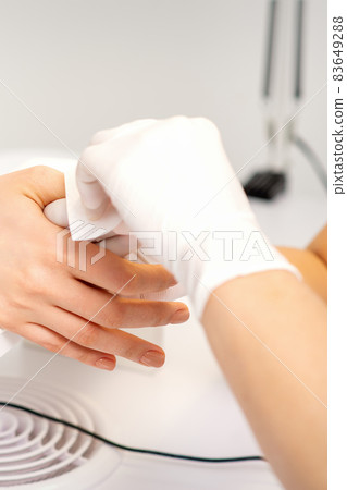 Hands of a manicurist in white protective gloves wipe female nails with a paper napkin in the salon. Hands of a manicurist in white protective gloves wipe female nails with a paper napkin in the salon. 83649288