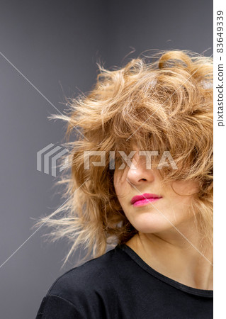 Portrait of beautiful young white woman with a curly light brown medium length hairstyle on dark background. 83649339