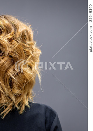 Back view of the woman with long brown curly hair stands on a dark background. 83649340