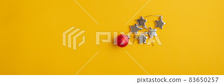 Red Christmas bauble and golden stars on yellow background Red Christmas bauble and golden stars on yellow background 83650257