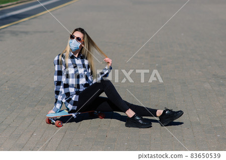 Portrait of a young female in a medical mask with longboard in the city during the quarantine Portrait of a young female in a medical mask with longboard in the city during the quarantine 83650539