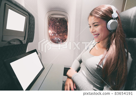 Passenger in airplane using tablet computer. Woman in plane cabin using smart device listening to music on headphones. Banner panorama travel people lifestyle. 83654191