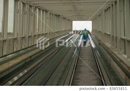 A woman in a raincoat rises on an escalator. Girl in protective clothing from the rain. Back view. 83655811