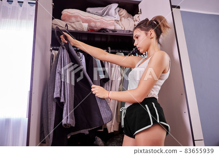 Woman chooses clothes in wardrobe. Young female changes clothing in dressing room. Woman chooses clothes in wardrobe. Young female changes clothing in dressing room. 83655939