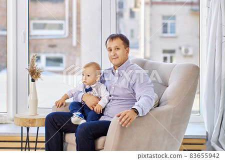 Toddler sits on his father lap in living room. 83655942