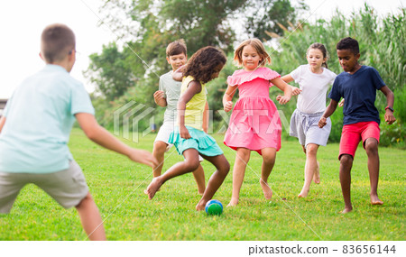 Happy preteen girls and boys playing football on green lawn 83656144