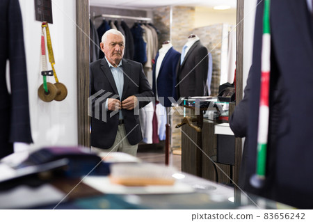 Elderly pensioner tries on new fashionable jacket in front of mirror in clothing store Elderly pensioner tries on new fashionable jacket in front of mirror in clothing store 83656242