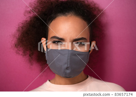 Questioning or studying look wearing reusable face mask African American charming girl in peachy t-shirt, to prevent others from corona COVID-19 and SARS cov 2 infection isolated on pink background 83657174