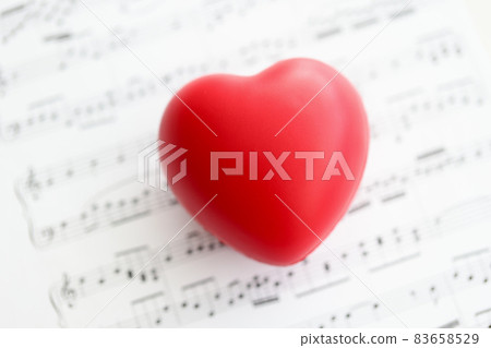 Red toy heart lying on paper with notes closeup Red toy heart lying on paper with notes closeup 83658529