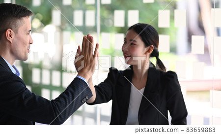 Two smiling business people giving each other high five for celebrating successful work project. Two smiling business people giving each other high five for celebrating successful work project. 83659883