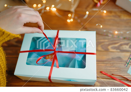 Close-up of woman's hand pulling ribbon from gift box. 83660042
