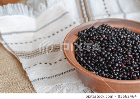 Ripe black elderberries in a brown bowl. Clay bowl on top of a linen ethnic tablecloth. 83662464