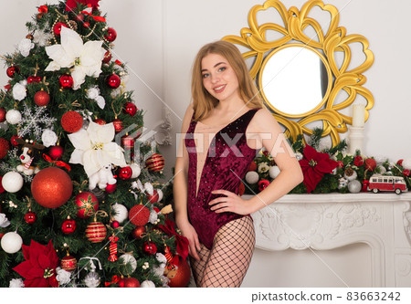 Beautiful, sexy female in red costume Snow Maiden, smiling, near many gifts on blue background. 83663242