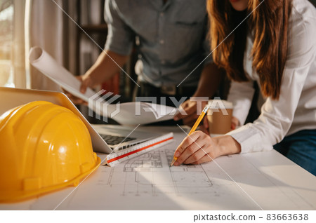 Creative architect projecting on the big drawings in the dark loft office or cafe in morning light. Creative architect projecting on the big drawings in the dark loft office or cafe in morning light. 83663638