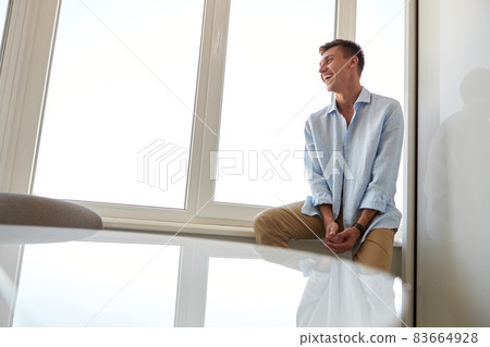 Happy beautiful handsome smiling caucasian man is relaxing at modern light home Happy beautiful handsome smiling caucasian man is relaxing at modern light home 83664928
