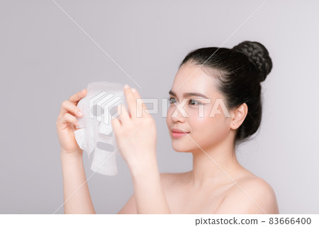 Beauty Skin Care Concept - Beautiful Caucasian Woman applying paper sheet mask on her face white background. Beauty Skin Care Concept - Beautiful Caucasian Woman applying paper sheet mask on her face white background. 83666400