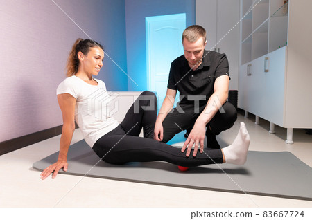 A young male massage therapist teaches a client Caucasian woman myofascial self-massage using a massage ball indoors. Myofasceal release A young male massage therapist teaches a client Caucasian woman myofascial self-massage using a massage ball indoors. Myofasceal release 83667724