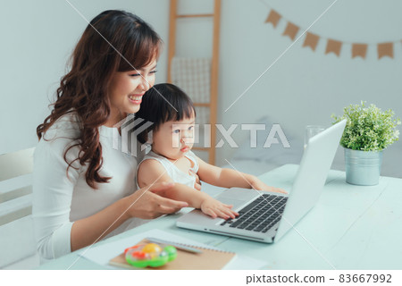 Working mother concept. Young woman working on laptop with her child from home 83667992