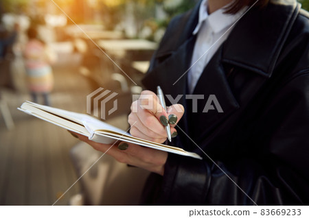Close-up of unrecognizable young business woman holding a pen and notepad, writing, making notes. 83669233