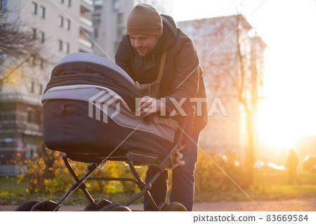 Happy young father with pram during the walk in nature Happy young father with pram during the walk in nature 83669584