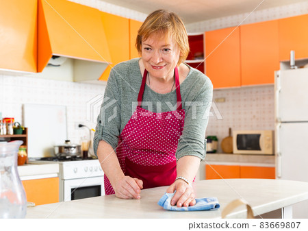 Elderly woman housewife in apron cleaning furniture at kitchen Elderly woman housewife in apron cleaning furniture at kitchen 83669807