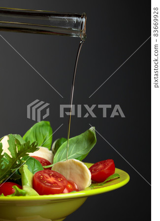 Mozzarella salad with tomatoes and herbs is watered with vegetable oil. 83669928