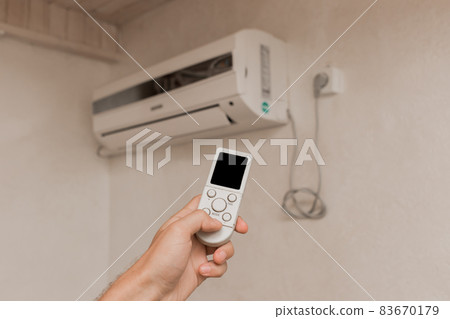 The guy's hand holds the remote control of the air conditioner. Cooling and temperature control in the room of the house 83670179