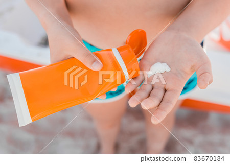 A young girl, holds sunscreen in her hands and is going to be smeared for protection from the sun against the background of the sea beach A young girl, holds sunscreen in her hands and is going to be smeared for protection from the sun against the background of the sea beach 83670184