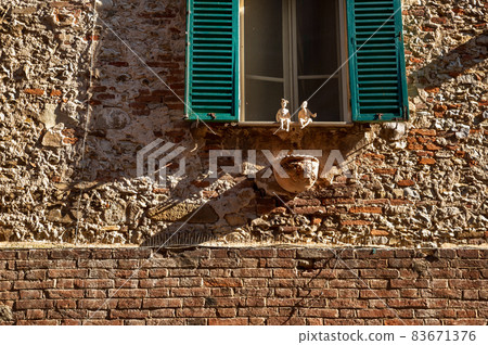 Castiglione del Lago Trasimeno, Umbria, Italy. August 2020. Amazing details of the facade of a house in the historic center: small statues animate the windows. Castiglione del Lago Trasimeno, Umbria, Italy. August 2020. Amazing details of the facade of a house in the historic center: small statues animate the windows. 83671376