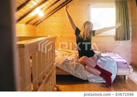 A beautiful girl lies on a bed in a room of a country house. Cozy wooden furniture creates comfort and coziness. Bare legs give a hint of eroticism. A beautiful girl lies on a bed in a room of a country house. Cozy wooden furniture creates comfort and coziness. Bare legs give a hint of eroticism. 83672096