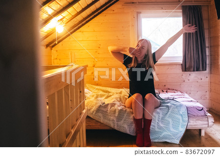 A beautiful girl lies on a bed in a room of a country house. Cozy wooden furniture creates comfort and coziness. Bare legs give a hint of eroticism. 83672097