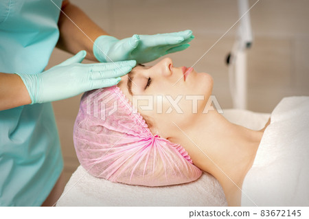 The woman is having cosmetic treatment during cosmetologist in medical gloves are touching the female face at the spa salon. 83672145