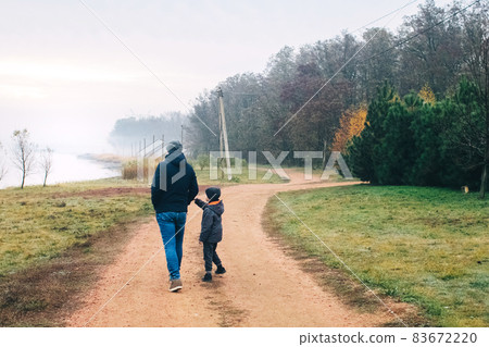Dad and son in forest. Family vacation among the autumn trees. Walk along a dirt road near the forest and a country house. The concept of having a pleasant time with your father and a happy childhood 83672220