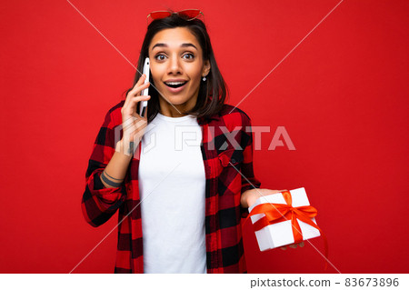 Shot of beautiful happy emotional young brunette woman isolated over red background wall wearing 83673896