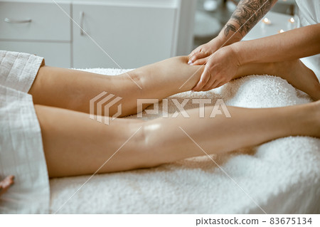 Professional caucasian specialist is doing leg message at modern minimalistic salon Professional caucasian specialist is doing leg message at modern minimalistic salon 83675134