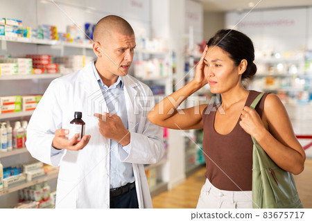 Oriental woman complaining about headache in chemist shop Oriental woman complaining about headache in chemist shop 83675717