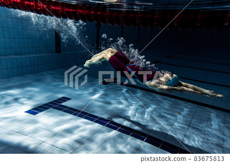 One female swimmer in swimming cap and goggles training at pool, indoors. Underwater view of swimming movements details. One female swimmer in swimming cap and goggles training at pool, indoors. Underwater view of swimming movements details. 83675813