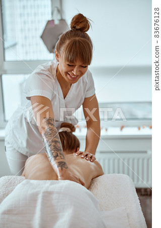 Professional confident massage master is doing procedures to caucasian woman in minimalistic modern cabinet 83676128