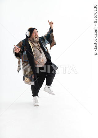 Fat stylish bearded tattoed caucasian man with big belly is posing and dancing wearing ethnic kimono 83676130