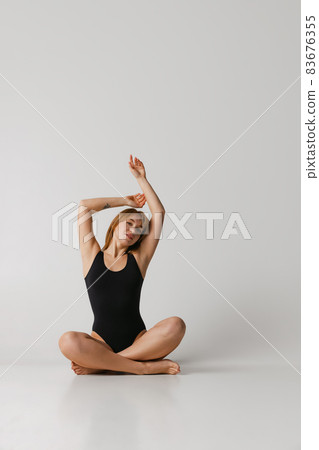 Young beautiful red-headed girl in black swimsuit sitting on floor isolated over gray studio background. Natural beauty concept. Young beautiful red-headed girl in black swimsuit sitting on floor isolated over gray studio background. Natural beauty concept. 83676355