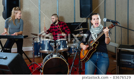 Attractive female soloist playing guitar and singing with her music band in sound studio Attractive female soloist playing guitar and singing with her music band in sound studio 83676529