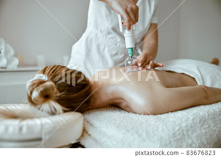 professional female specialist is doing cupping therapy on the back of beautiful caucasian lady 83676823