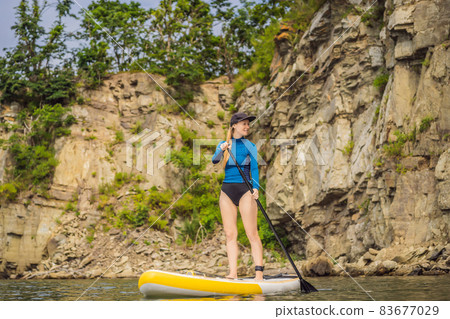 Young women Having Fun Stand Up Paddling in the sea. SUP. Red hair girl Training on Paddle Board near the rocks 83677029
