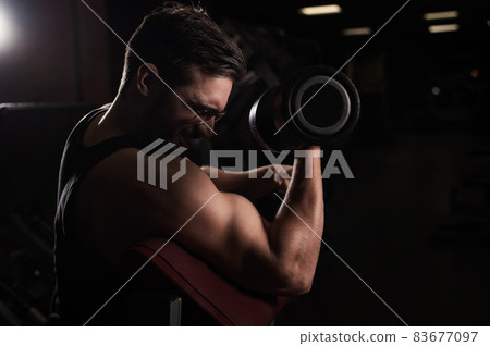 A handsome man with glasses doing an exercise for biceps with a barbell. The guy is engaged in bodybuilding. Trainer in the gym with muscular arms. A handsome man with glasses doing an exercise for biceps with a barbell. The guy is engaged in bodybuilding. Trainer in the gym with muscular arms. 83677097