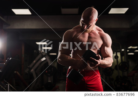 Shirtless handsome man doing biceps and chest exercise with dumbbell. Macho guy bodybuilder. Muscular trainer in the gym. 83677696