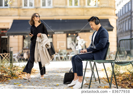 Businessman work on laptop and woman go in city Businessman work on laptop and woman go in city 83677938