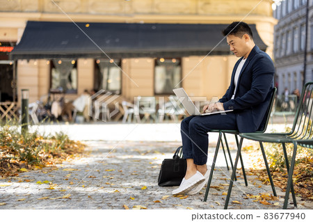 Businessman typing on laptop during work outdoors Businessman typing on laptop during work outdoors 83677940