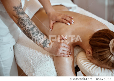 Professional confident massage master is doing procedures to caucasian woman in minimalistic modern cabinet Professional confident massage master is doing procedures to caucasian woman in minimalistic modern cabinet 83678082