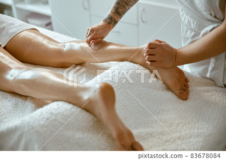 Massagist woman is doing professional leg massage in modern salon 83678084